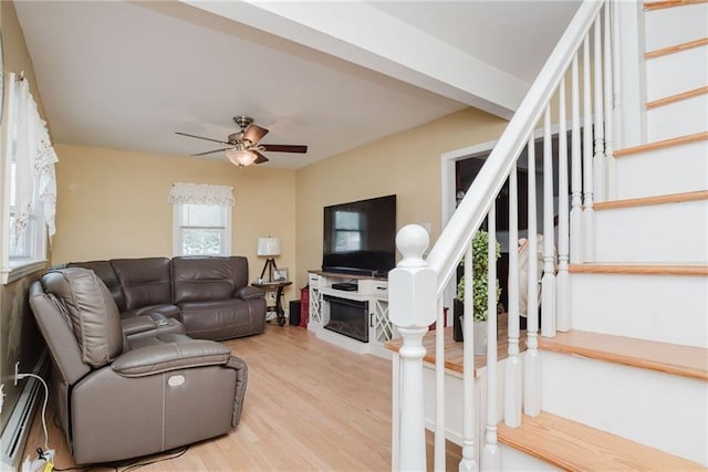 living room with stairway, a glass covered fireplace, light wood-type flooring, and a ceiling fan