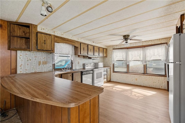 kitchen with a peninsula, wallpapered walls, light wood-style floors, and white appliances