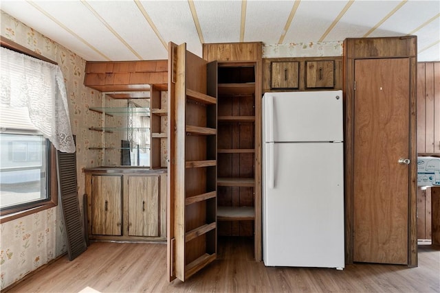 kitchen with freestanding refrigerator, light wood-type flooring, wallpapered walls, and brown cabinets