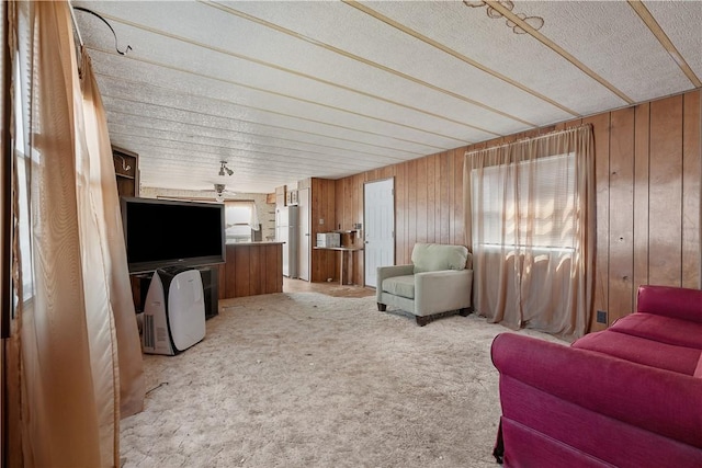 living area featuring ceiling fan, light carpet, a textured ceiling, and wooden walls