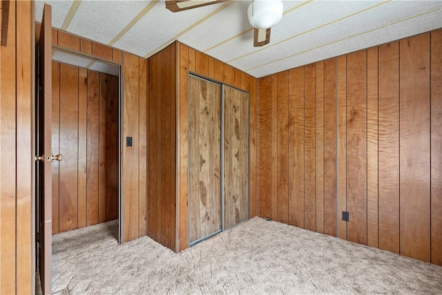 unfurnished bedroom featuring carpet flooring, wood walls, and ceiling fan