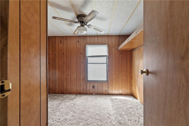 carpeted spare room with a textured ceiling, a ceiling fan, and wood walls