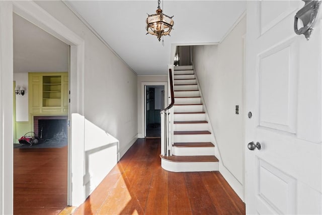 stairs featuring wood finished floors, baseboards, crown molding, a brick fireplace, and a notable chandelier