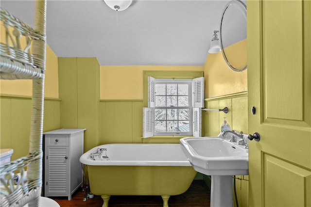 bathroom featuring a decorative wall, a soaking tub, a wainscoted wall, and wood finished floors
