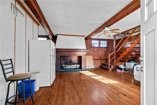 unfurnished living room with wood walls, hardwood / wood-style flooring, stairway, a brick fireplace, and beamed ceiling