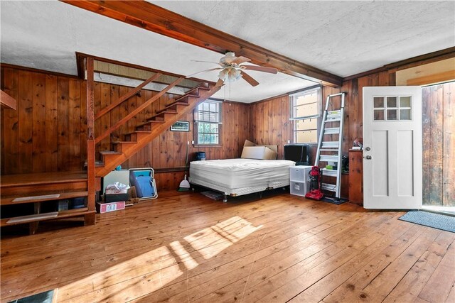 bedroom featuring beam ceiling, wooden walls, wood-type flooring, and a textured ceiling