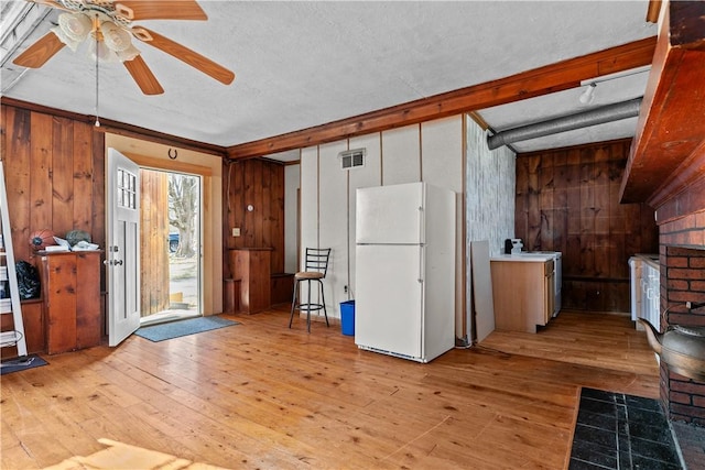 interior space featuring freestanding refrigerator, wood walls, and light wood-style floors