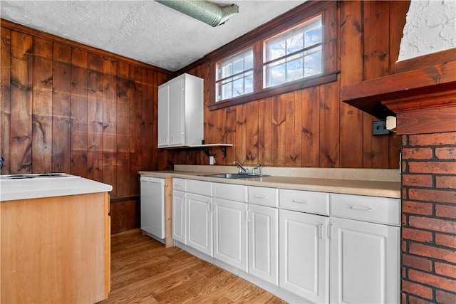 clothes washing area with light wood-style floors, a textured ceiling, wooden walls, and a sink