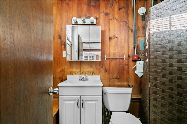 bathroom featuring toilet, wooden walls, and vanity
