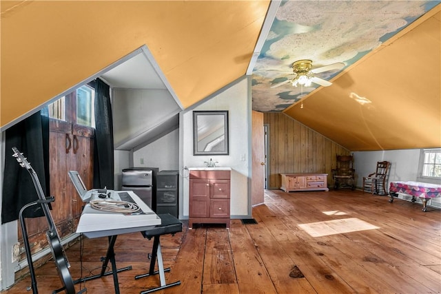 additional living space with a sink, lofted ceiling, hardwood / wood-style flooring, wooden walls, and a ceiling fan