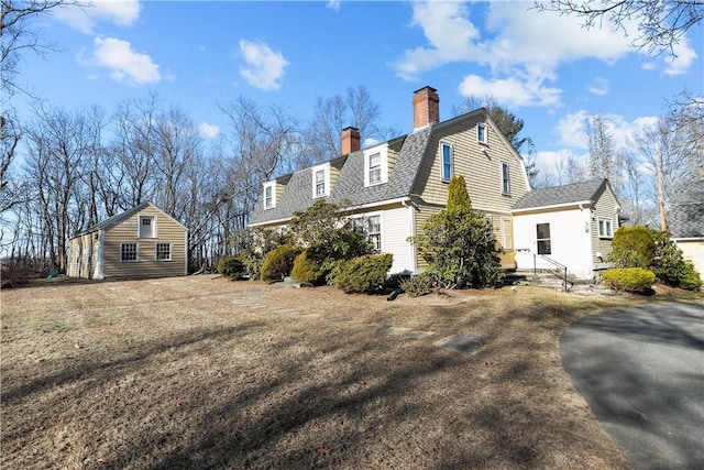 view of home's exterior with a gambrel roof, a chimney, a shingled roof, and an outbuilding