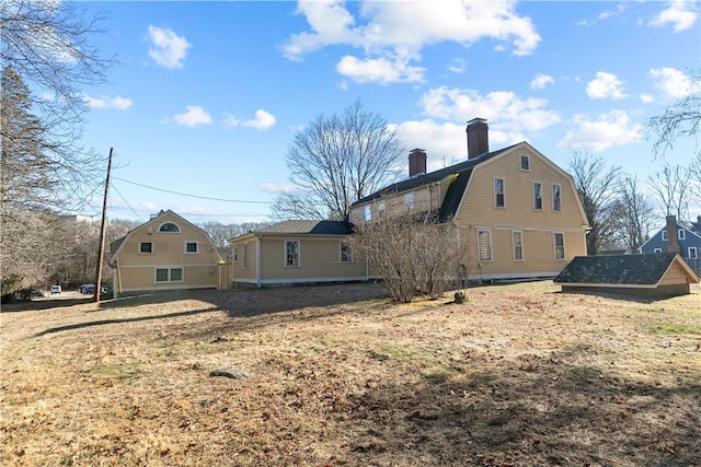 rear view of property featuring a gambrel roof and a chimney