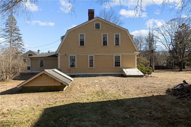 back of property featuring a chimney, a gambrel roof, and a lawn