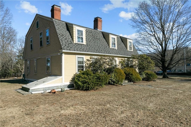 back of property with a chimney, a gambrel roof, and roof with shingles