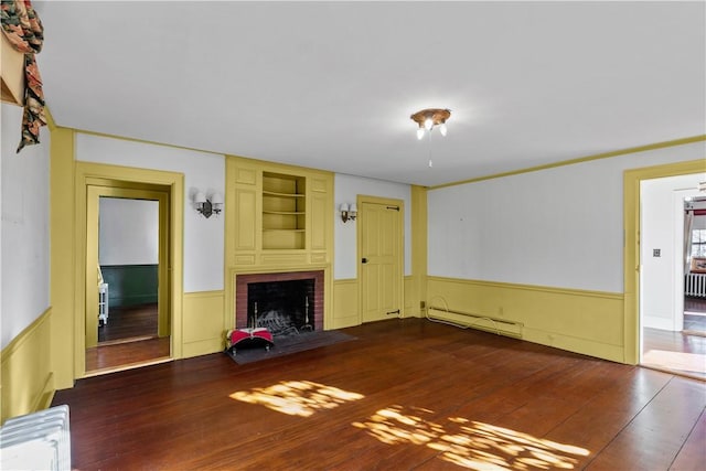 unfurnished living room featuring hardwood / wood-style floors, a baseboard radiator, a brick fireplace, and a wainscoted wall