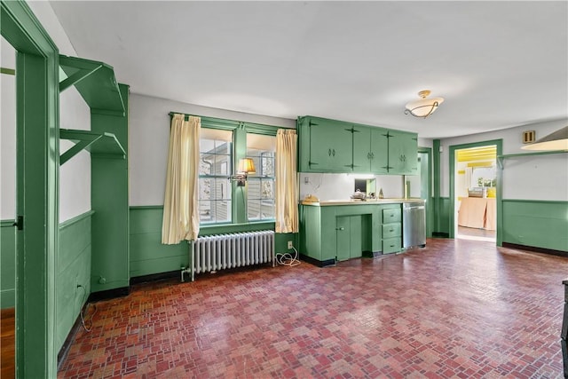 kitchen with brick patterned floor, dishwasher, radiator heating unit, a wainscoted wall, and green cabinetry