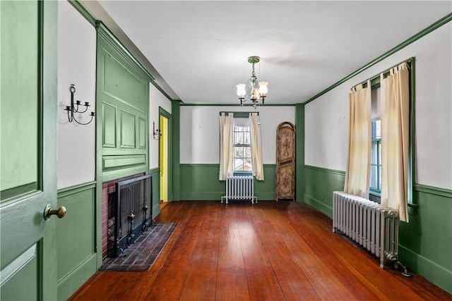 unfurnished dining area featuring radiator heating unit, a chandelier, dark wood-type flooring, a wainscoted wall, and crown molding