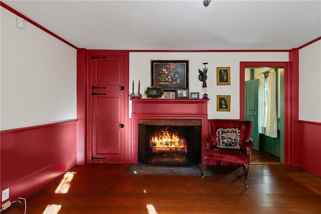 living area with crown molding, a fireplace with flush hearth, and hardwood / wood-style flooring
