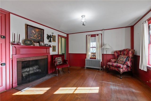 living area with radiator heating unit, wainscoting, wood finished floors, healthy amount of natural light, and a brick fireplace