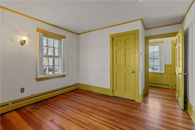 spare room with ornamental molding, baseboard heating, and light wood-type flooring