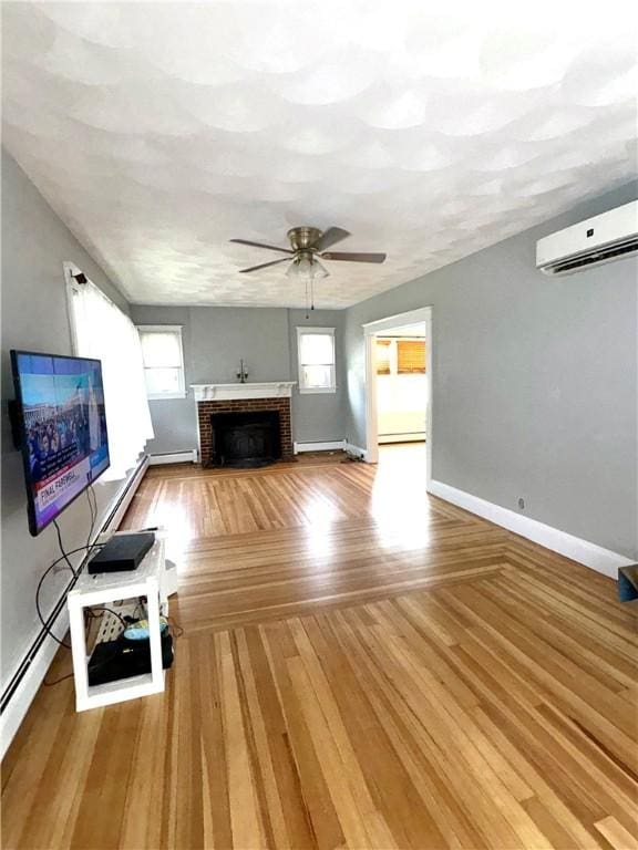 unfurnished living room with a ceiling fan, a wall mounted air conditioner, baseboards, wood finished floors, and a fireplace