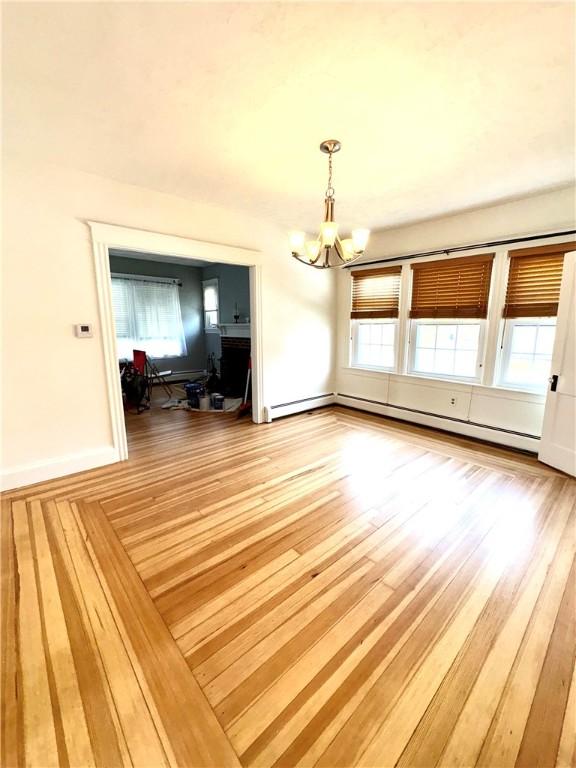 unfurnished dining area with light wood-style flooring, baseboard heating, and a notable chandelier