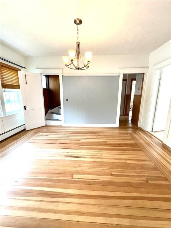 unfurnished dining area featuring a notable chandelier, baseboard heating, and light wood-style floors