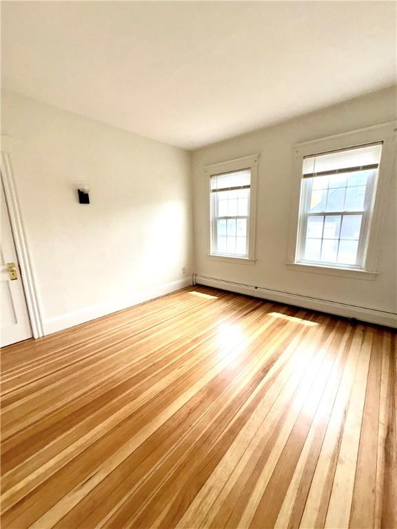 empty room with a baseboard heating unit, baseboards, and hardwood / wood-style flooring