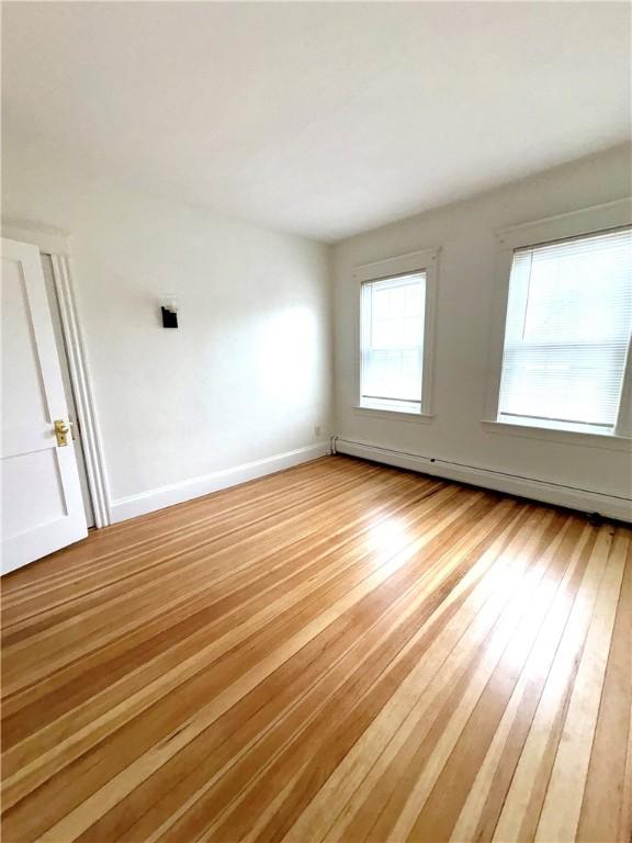 unfurnished room featuring wood finished floors, baseboards, and a baseboard heating unit