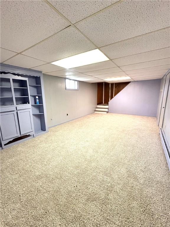 below grade area with carpet flooring, built in shelves, and a paneled ceiling