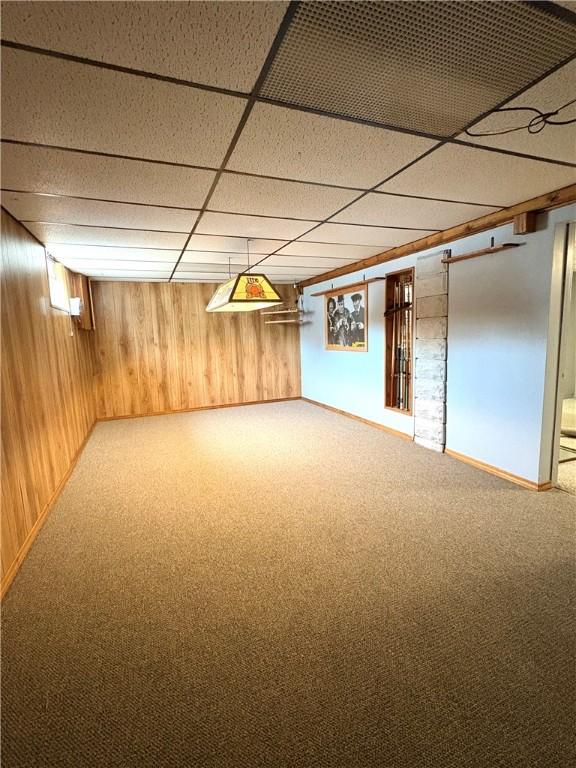 finished below grade area featuring a drop ceiling, wood walls, and carpet floors