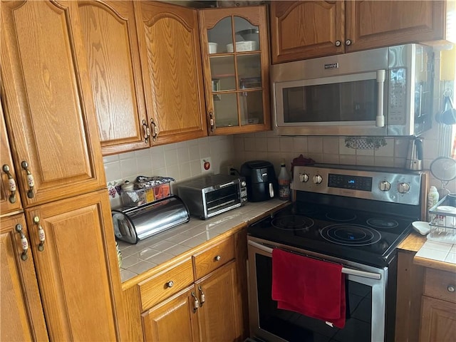 kitchen featuring appliances with stainless steel finishes, glass insert cabinets, tile counters, and backsplash