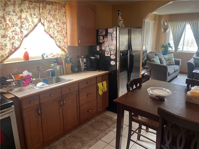 kitchen featuring light tile patterned floors, brown cabinetry, stainless steel refrigerator with ice dispenser, backsplash, and tile countertops