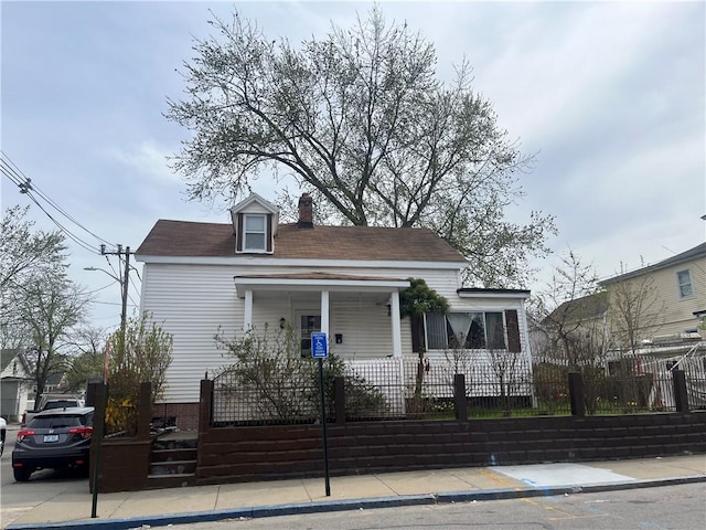 view of front of property featuring covered porch, a fenced front yard, and a chimney
