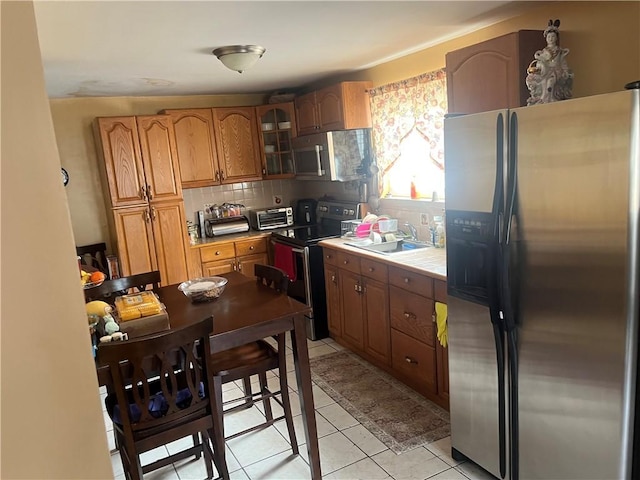 kitchen featuring a sink, stainless steel appliances, tasteful backsplash, brown cabinets, and tile counters
