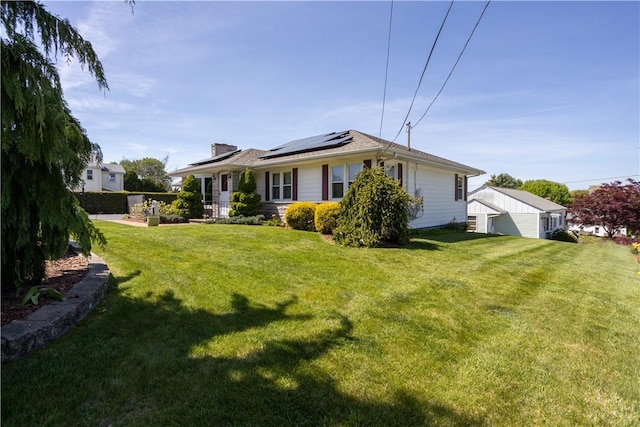 back of property with roof mounted solar panels, a yard, a chimney, and a detached garage