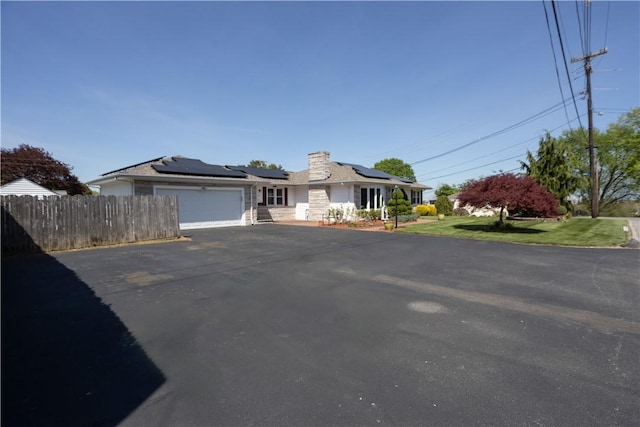 view of front of home with a chimney, fence, solar panels, a garage, and aphalt driveway