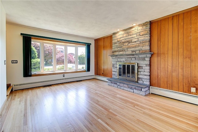 unfurnished living room with a fireplace, wood walls, baseboard heating, and wood finished floors
