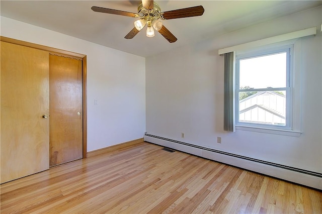 unfurnished bedroom with light wood-style flooring, a ceiling fan, and a baseboard heating unit