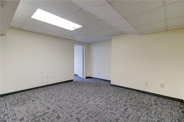 spare room with baseboards, dark carpet, and a paneled ceiling