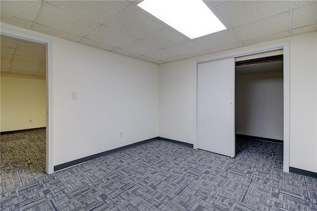 unfurnished bedroom featuring carpet, a closet, baseboards, and a paneled ceiling