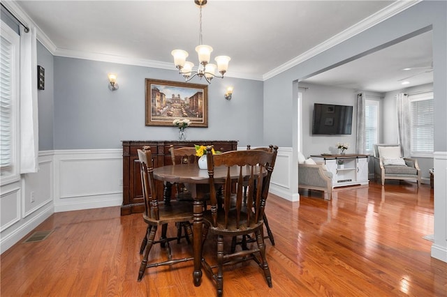 dining space featuring wood finished floors, a chandelier, crown molding, and a wainscoted wall