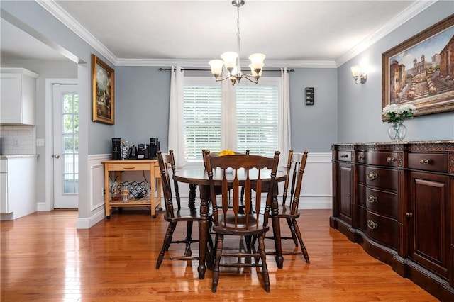 dining room with a chandelier, light wood-style floors, a wainscoted wall, crown molding, and a decorative wall