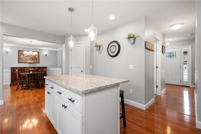 kitchen with light wood finished floors, a kitchen breakfast bar, white cabinets, a center island, and decorative light fixtures