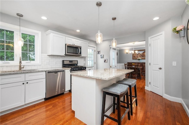 kitchen featuring appliances with stainless steel finishes, a sink, white cabinets, a center island, and tasteful backsplash