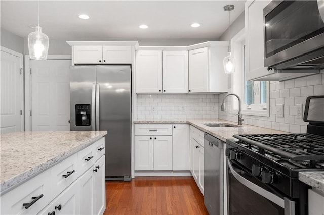 kitchen with stainless steel appliances, a sink, white cabinets, decorative light fixtures, and light stone countertops