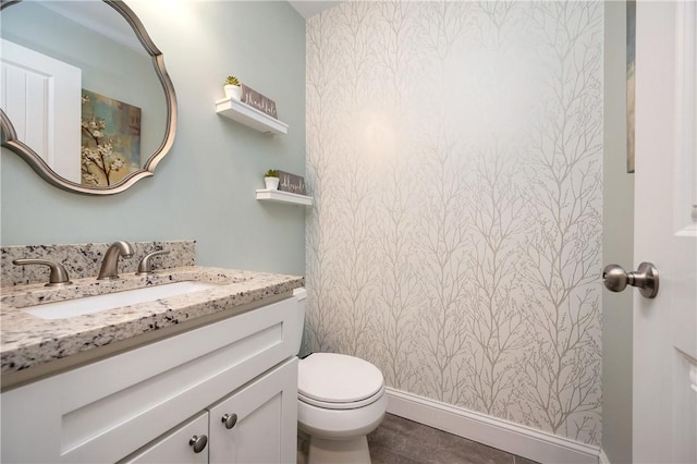 bathroom featuring vanity, toilet, wallpapered walls, and baseboards