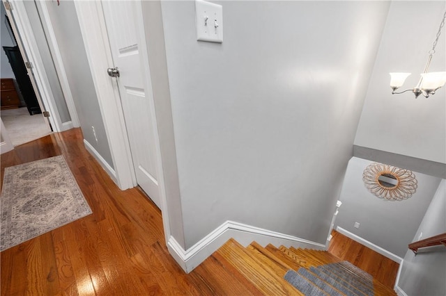 staircase featuring wood finished floors, baseboards, and a chandelier