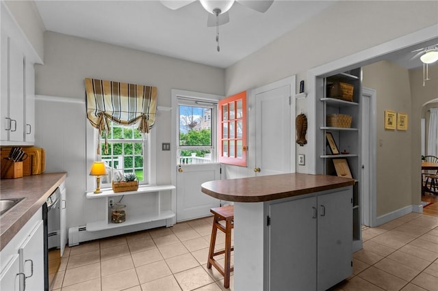 kitchen featuring a ceiling fan, light tile patterned floors, dark countertops, a baseboard radiator, and dishwashing machine