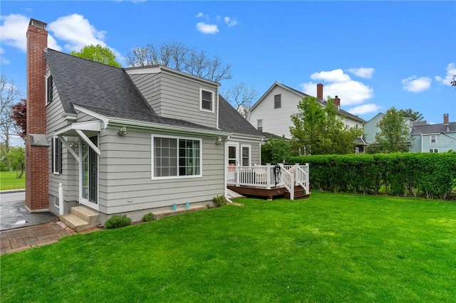 rear view of property with a deck, a yard, roof with shingles, and a chimney